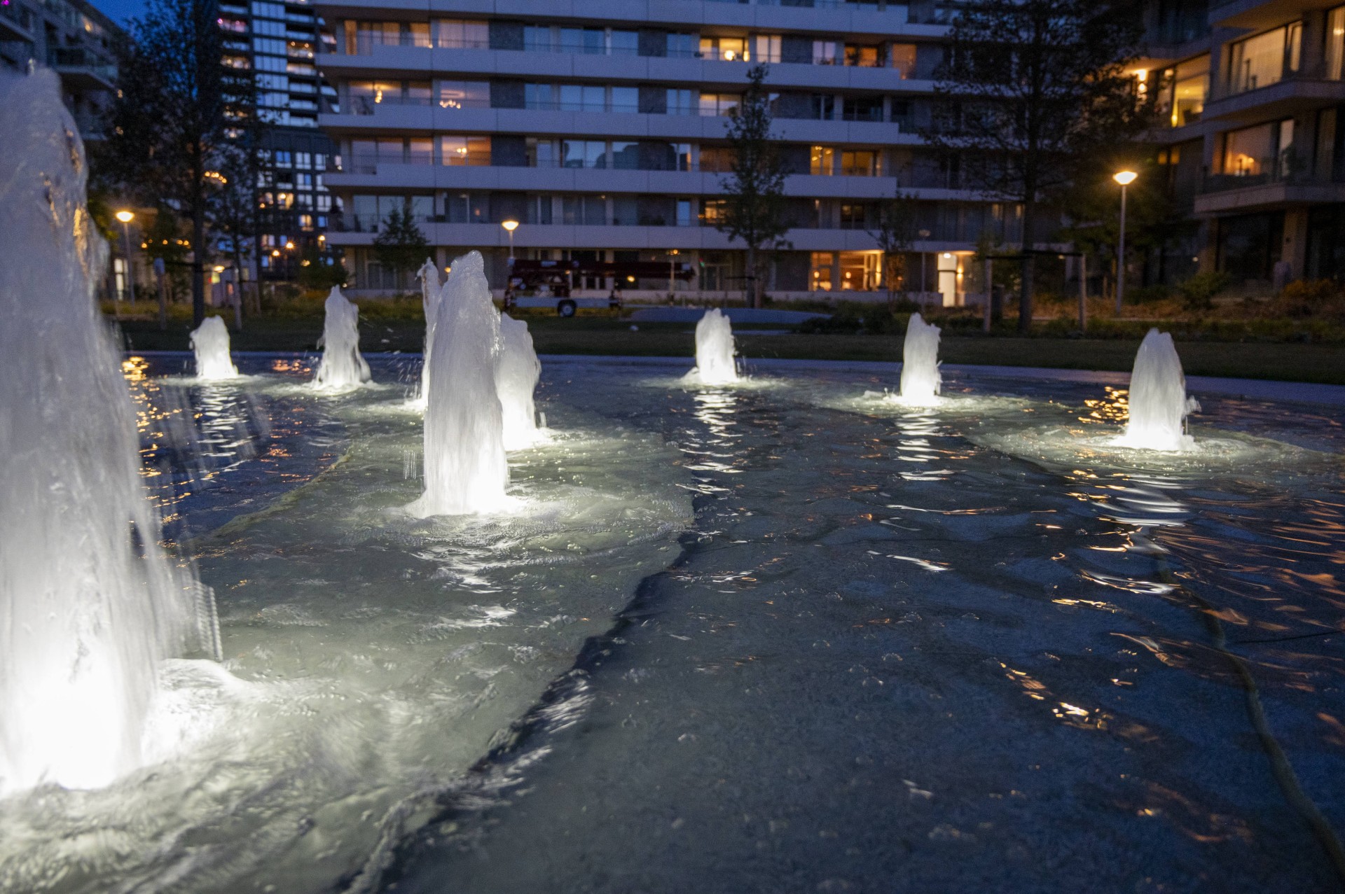 Verlichte spuiters van de fontein met woongebouwen op de achtergrond in de avond
