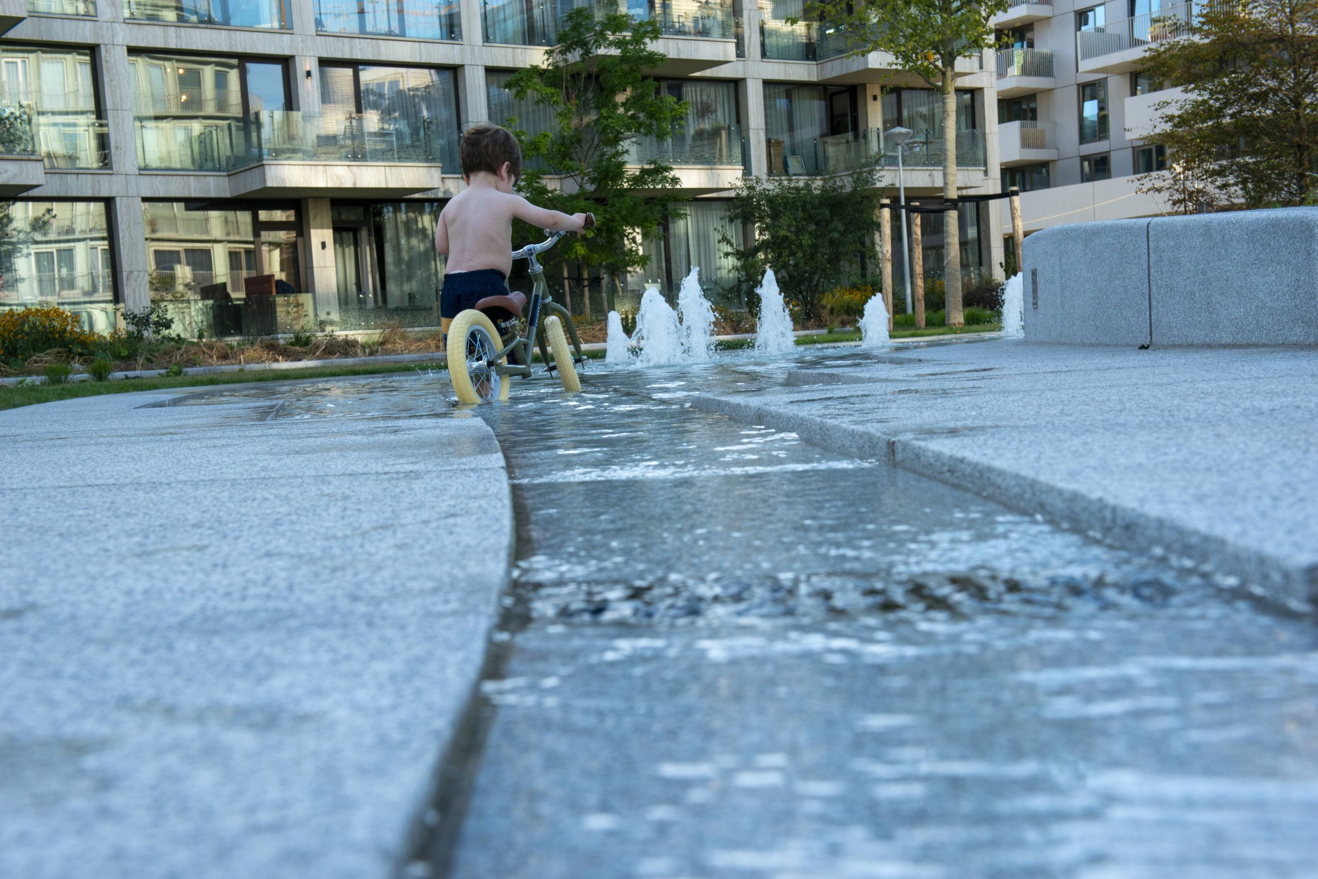 Kind fietst door de waterlaag van de fontein op het Buurtplein in Overhoeks