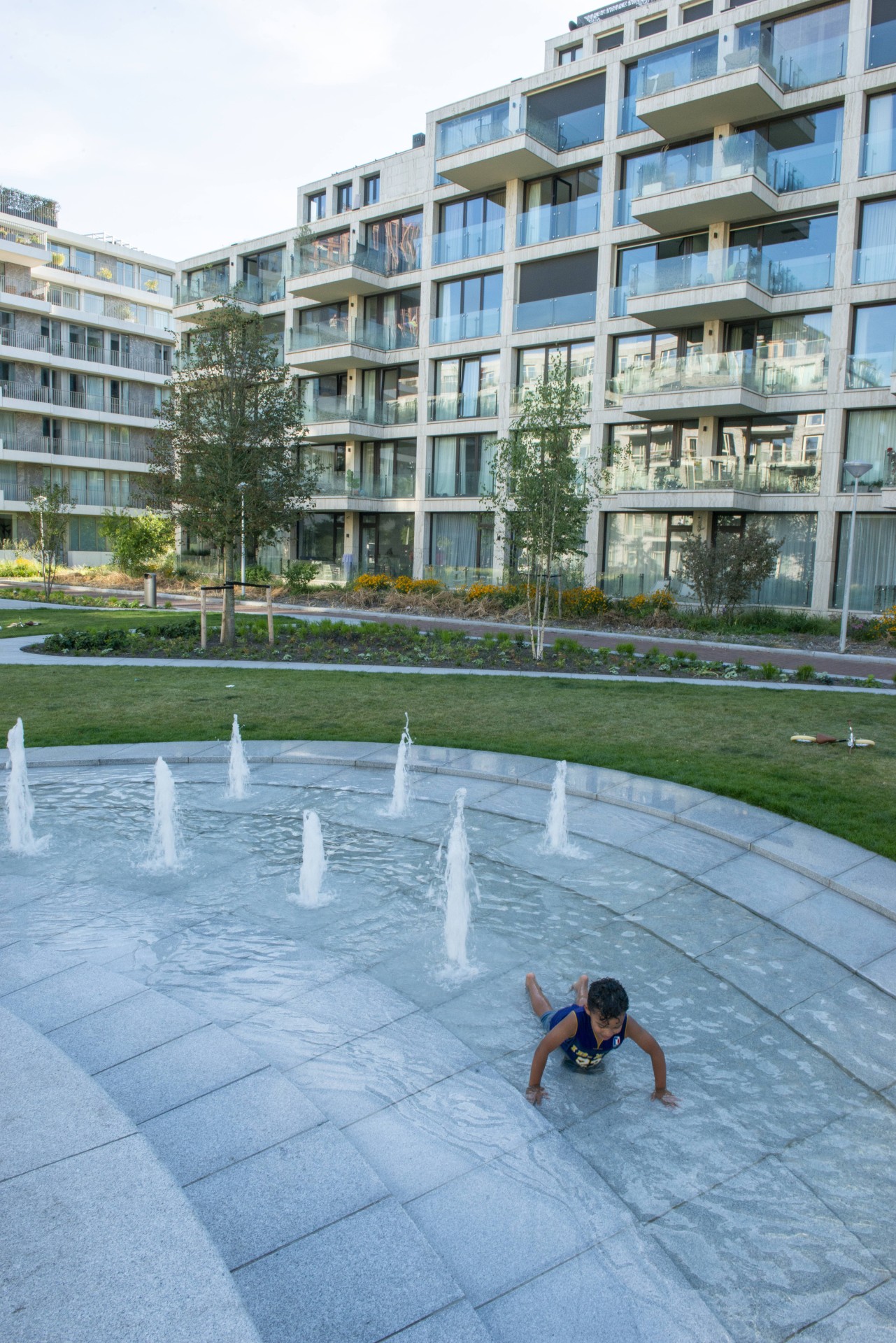 Een kind speelt in de waterlaag van de fontein op het Buurtplein in Overhoeks