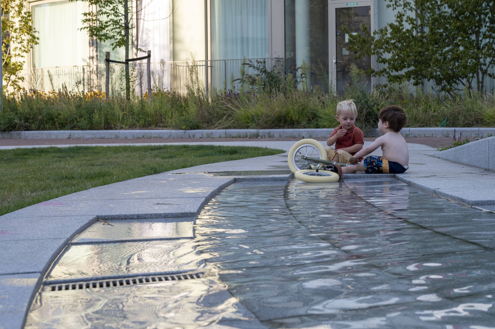 Kinderen zitten in de natuurstenen goot met water op het Buurtplein in Overhoeks
