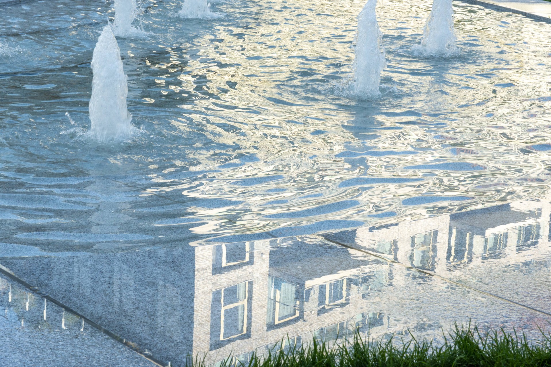 Spuiters en waterlaag in graniet met de reflectie van een woongebouw op het Buurtplein