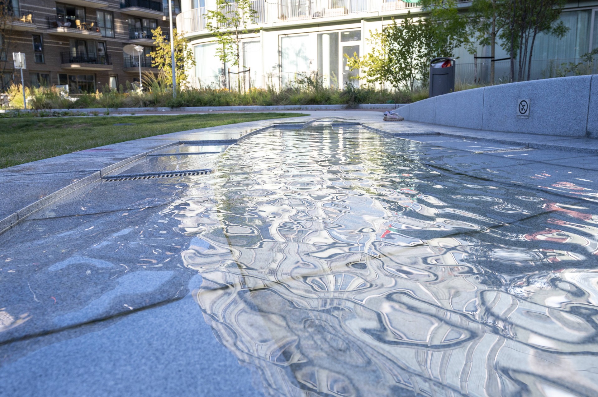 Waterlaag in graniet met reflecties op het Buurtplein in Overhoeks
