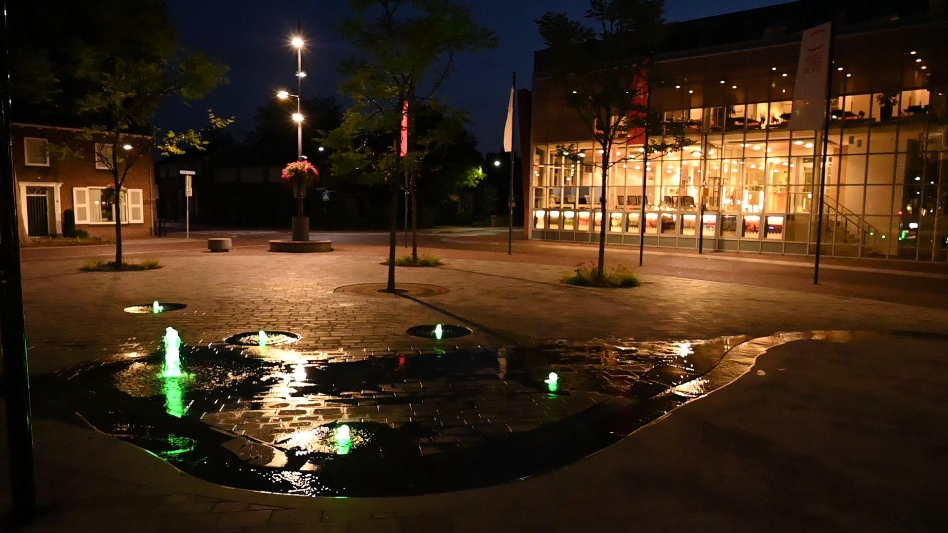 Groen verlichte fonteinen in de waterloop op het Louis Jansenplein in Cuijk 's avonds