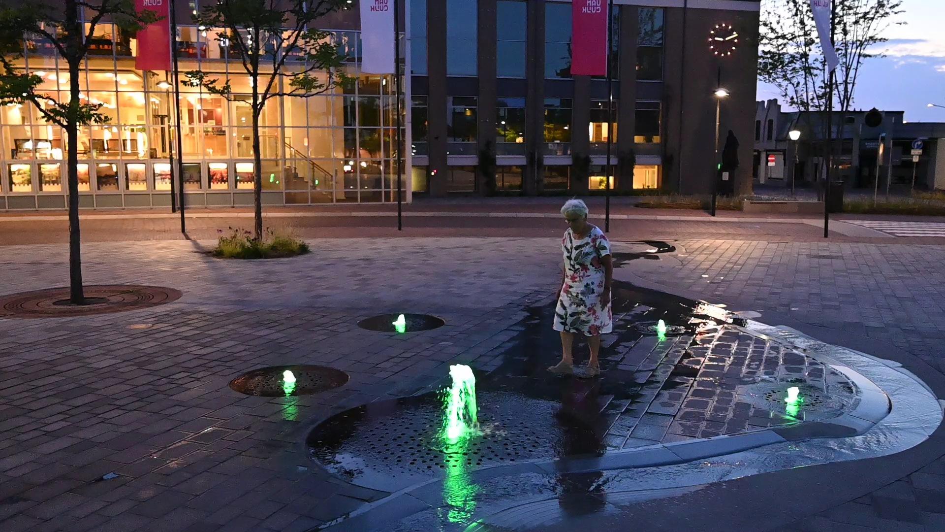 Bezoeker bij de groen verlichte fonteinen en de waterloop voor het gemeentehuis in Cuijk