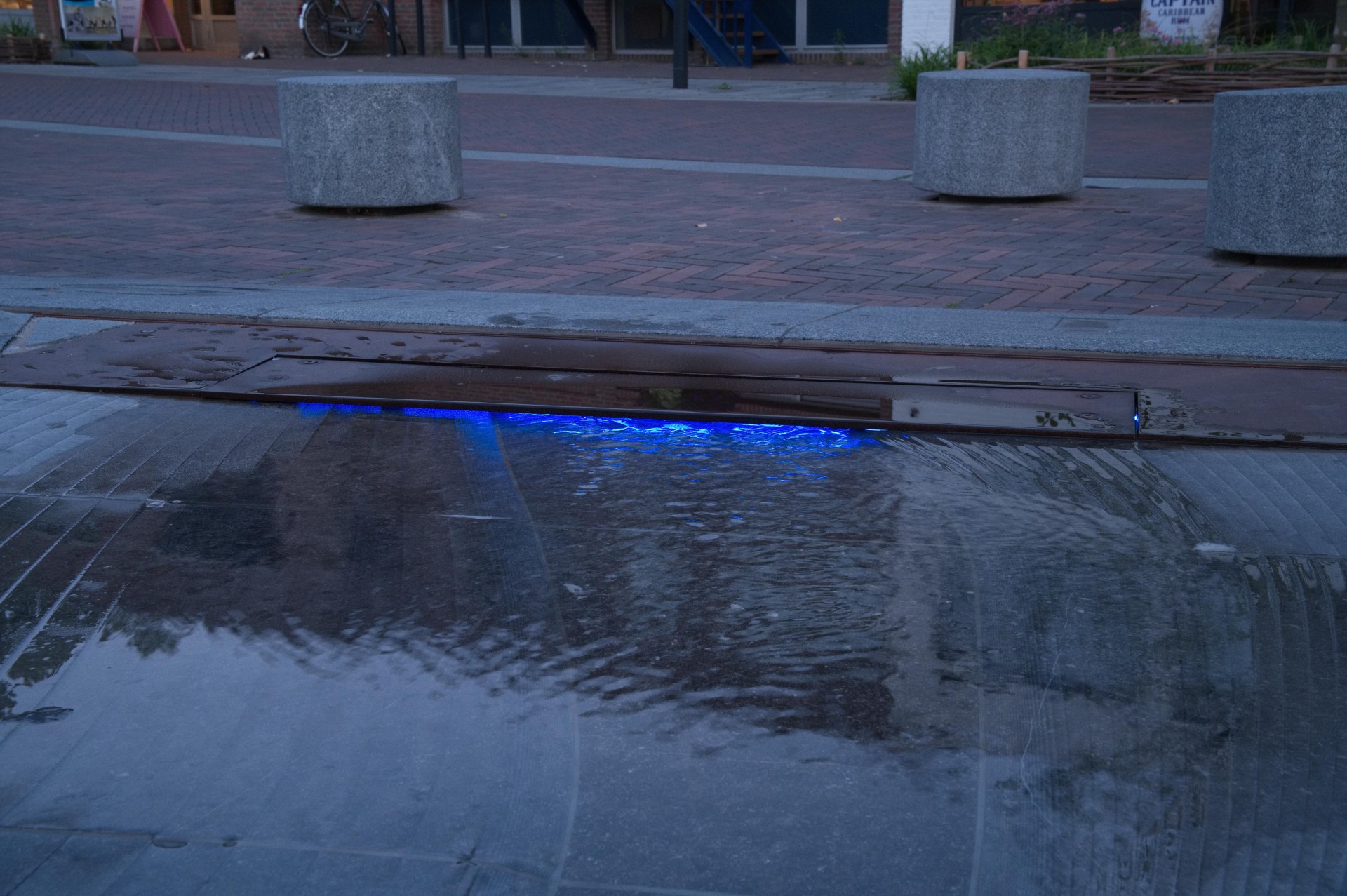 Water stroomt in de schemering over cortenstaal en hardsteen met blauwe ledverlichting in Cuijk