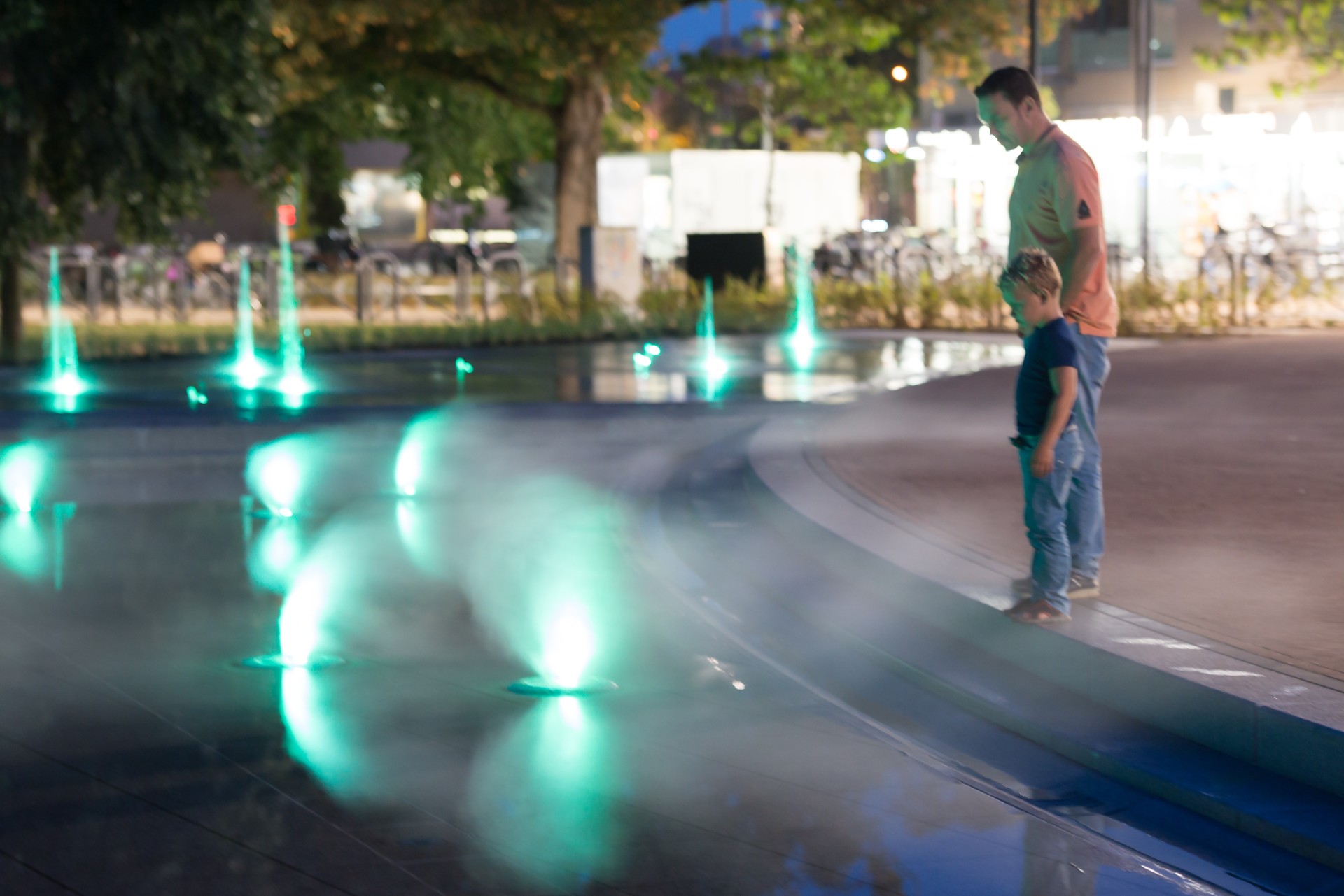 Doetinchem: vader en kind bij een verlichte waterspeelplaats in de avond