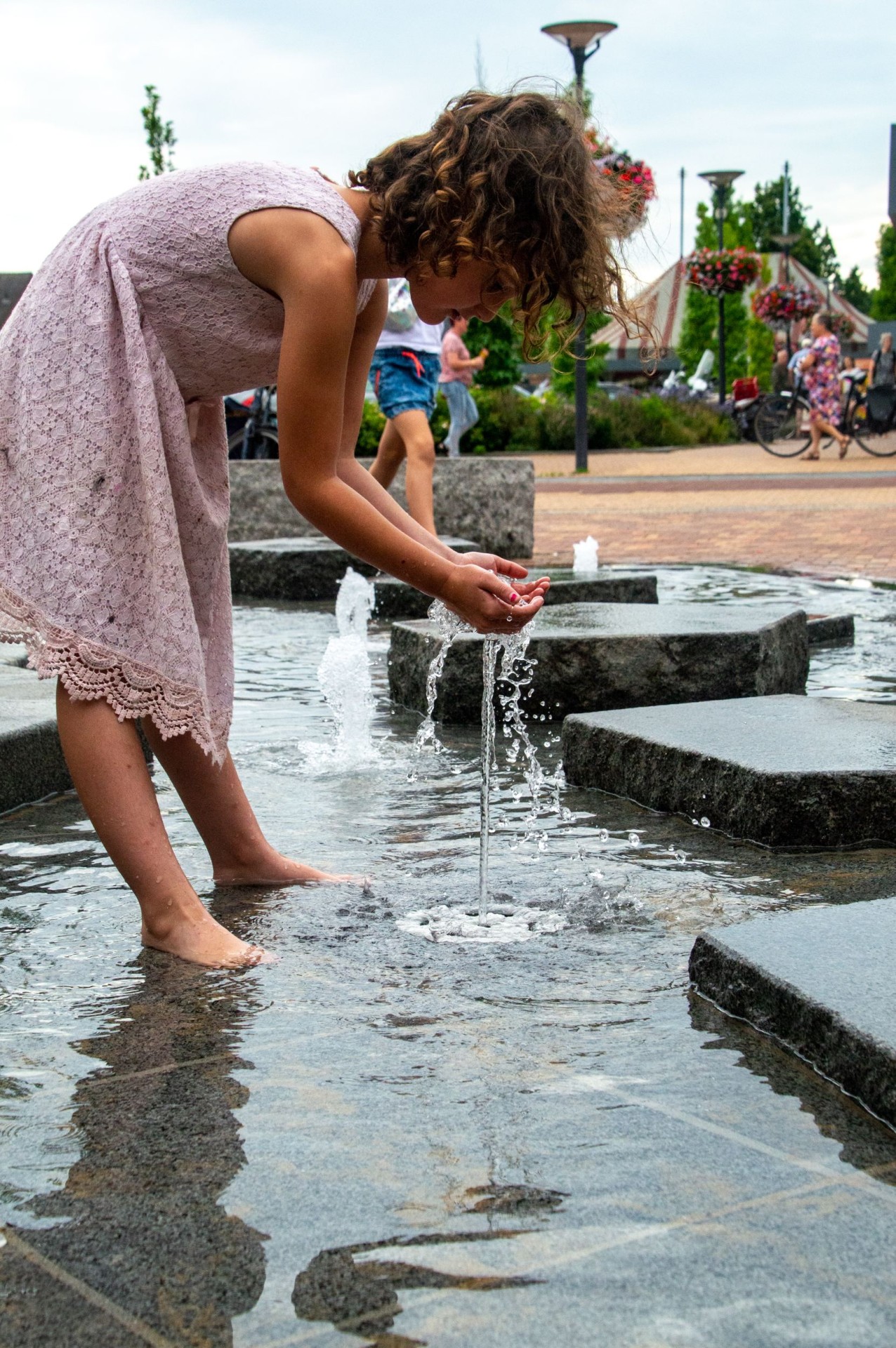Meisje schept water met haar handen bij de ijsschotsen van de fontein in Dieren