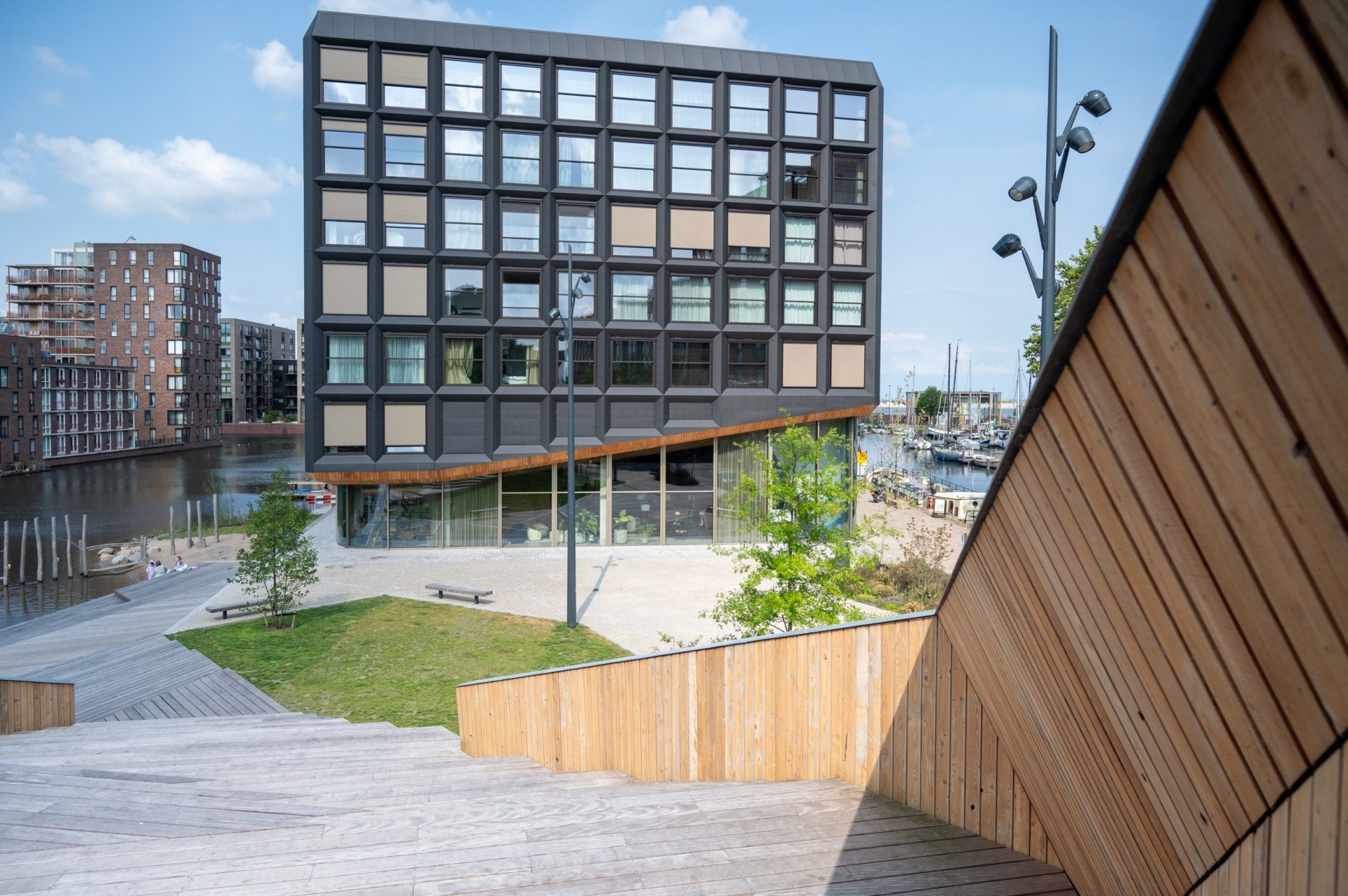 Houten wand, vlonders en gazon met het woongebouw Jonas en de haven op de achtergrond