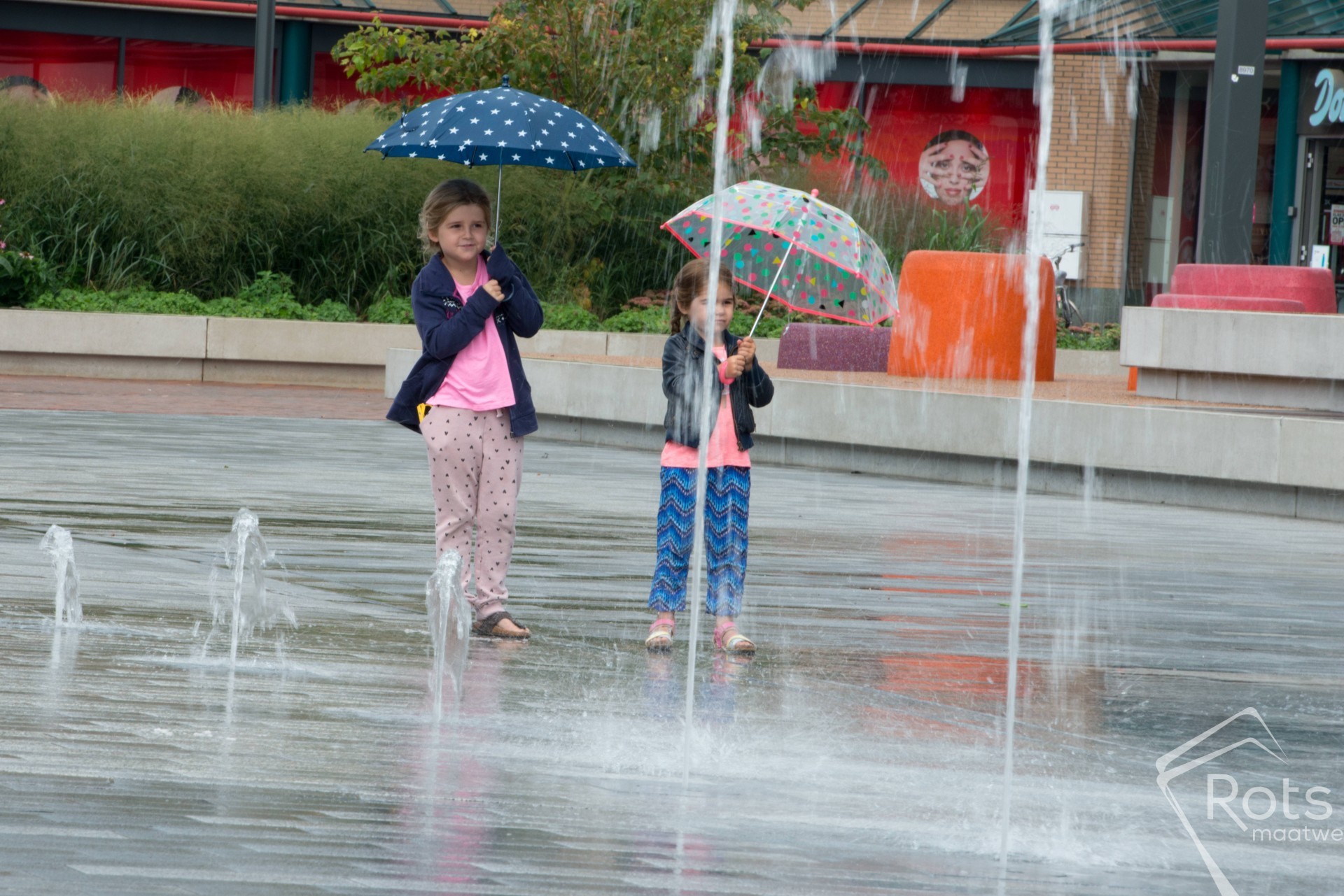 Twee kinderen met een paraplu spelen in de fonteinen op de Nieuwe Markt in Roosendaal