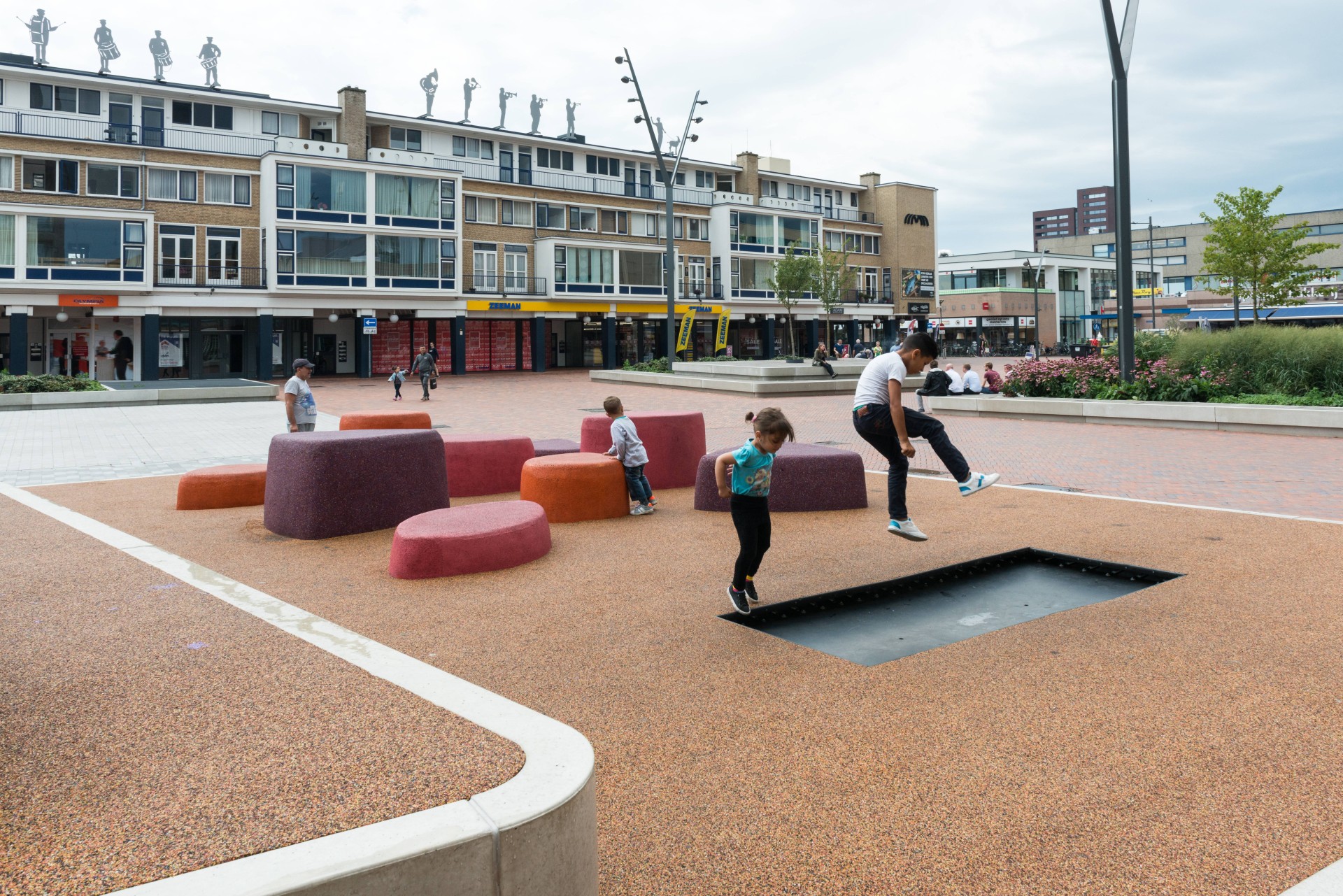 Kinderen spelen op de speelelementen bij een groen eiland met betonnen zitrand op de Nieuwe Markt in Roosendaal